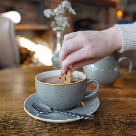 A hand dunking a biscuit in a hot drink