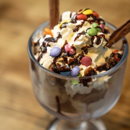 A Candy Mania dessert in a sundae glass on a wooden table.