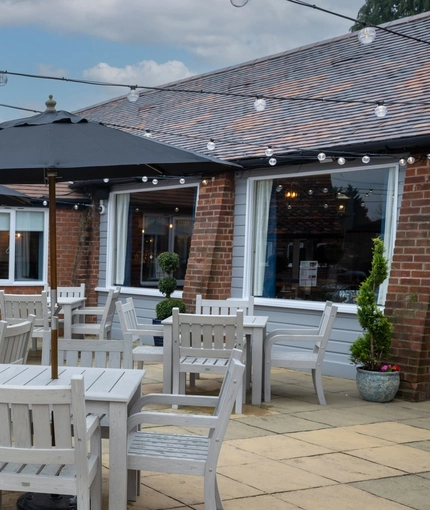 A paved exterior seating area at The Vine Inn, with wooden tables and chairs, shade umbrellas, and string lights overhead.