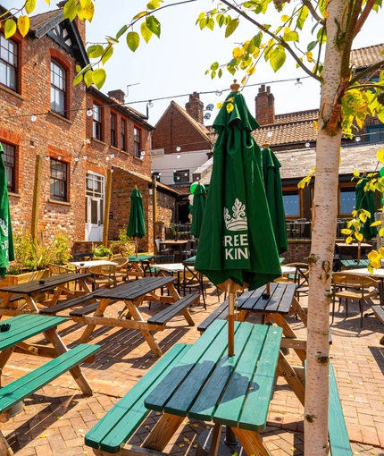 The exterior paved beer garden seating area at The Windmill Inn in York, with wooden picnic tables, shade umbrellas, and string lights overhead.