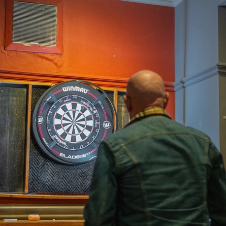 Noel playing darts in the gaming area at the Lord Derby.