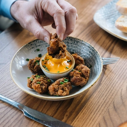 A hand taking a piece of food from a bowl on a wooden table.