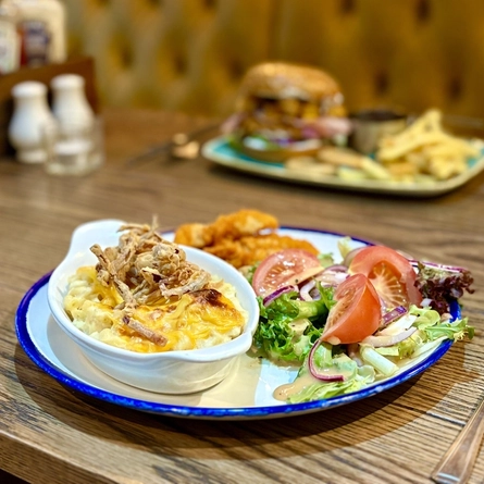 Plated dishes for Burger of the Month October served at Greene King Pubs.  One is a roasting dish of Macaroni Cheese and a plated chicken burger.
