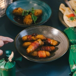A hand about to take a pig in blanket from a bowl on a festive decorated table.