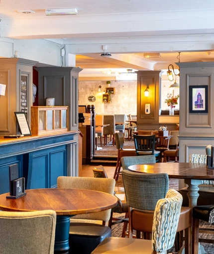 Interior dining area of a pub with a bar and a TV playing sports.