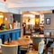 Interior dining area of a pub with a bar and a TV playing sports.