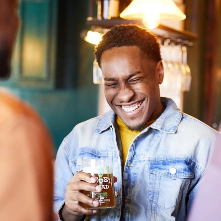 Three people in a pub bar area, one of them laughing while holding a glass of Level Head IPA.