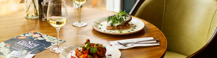 An image focusing on 2 Starter dishes and 2 glasses of white wine from the Set menu sat on a table within the interior restaurant seating area at a Chef & Brewer venue.