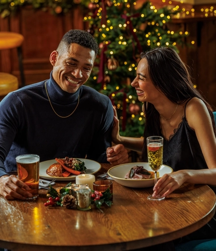 An image of 2 people enjoying various festive main dishes and drinks within the interior restaurant seating area during Christmas time at The Watermill.