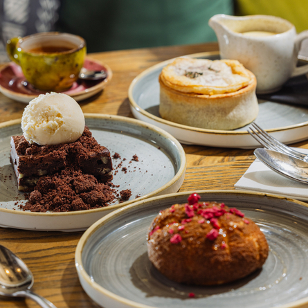 An advertising image showing a selection of desserts from the Prix Fixe menu sat on a table within the interior restaurant seating area at The Four Oaks.