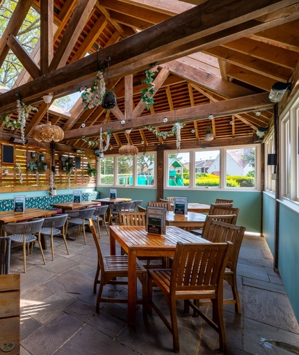 The exterior under cover seating area at The Walkford, with string lights and flowers hanging from the vaulted ceiling, potted plants and chalkboards on the wooden wall, and padded bench seats along one wall.