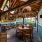 The exterior under cover seating area at The Walkford, with string lights and flowers hanging from the vaulted ceiling, potted plants and chalkboards on the wooden wall, and padded bench seats along one wall.