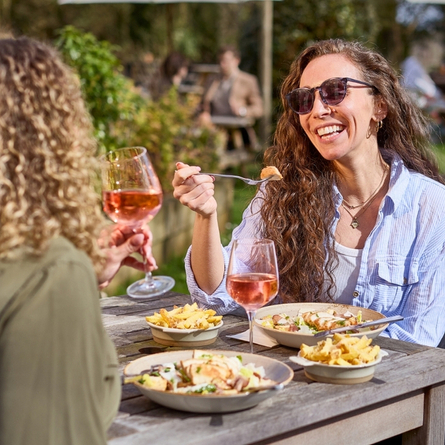 A banner showing 2 people sat at a table enjoying mains dishes with sides and glasses of rose wine within the exterior beer garden seating area at a Chef & Brewer venue.