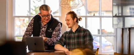 two men sat at a table looking at a laptop