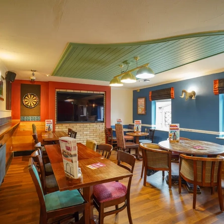 Interior dining area of a pub with a TV and a dartboard.