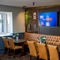 An interior restaurant seating area at the Rudds Arms; with a long, upholstered booth seat; and a large TV, framed artwork, and artificial plants on the wall above it.