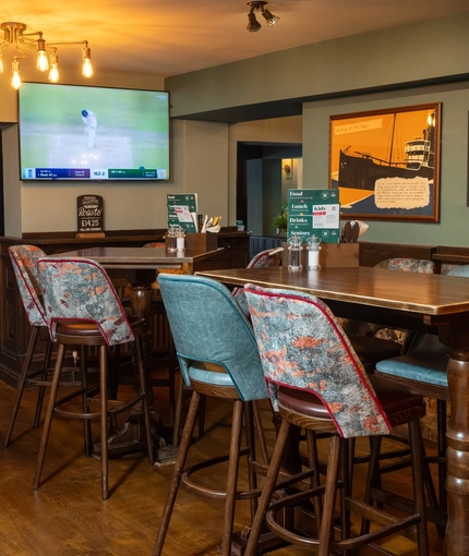 An interior restaurant seating area at The Ship in Bedford; with framed artwork, wood panelling, and a TV on the wall.