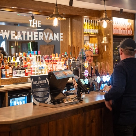 A member of staff serving two guests at the bar inside the Weathervane.