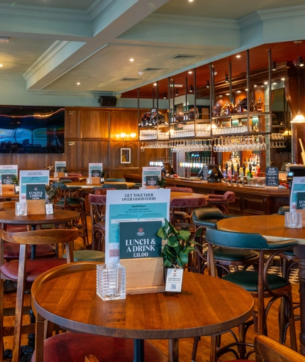 The bar and interior restaurant seating area of the Blue Posts in St James's, with a TV on the wood panelled wall, and glasses hanging in racks above the bar.