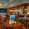 The bar and interior restaurant seating area of the Blue Posts in St James's, with a TV on the wood panelled wall, and glasses hanging in racks above the bar.