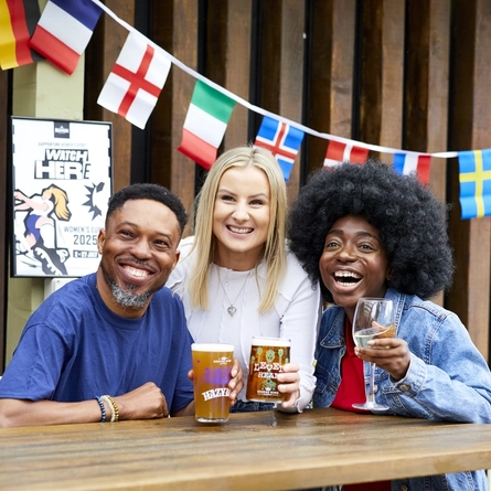 A mixed group of people sitting at an outdoor table, enjoying watching sport and drinks.