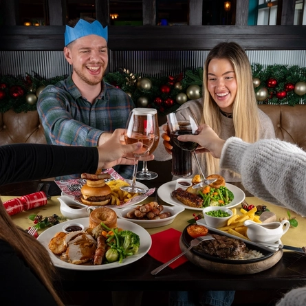 An interior shot of people celebrating Christmas and enjoying festive food in the restaurant/seating area at a Flaming Grill venue.