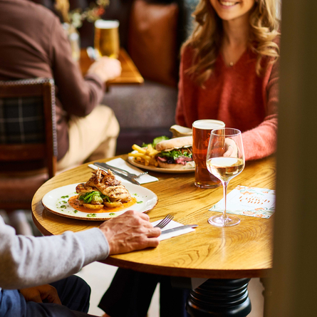 An image of 2 customers sat at a table within the interior restaurant seating area enjoying lunch dishes and drinks from the Lunch & Drink menu at a Chef & Brewer venue.