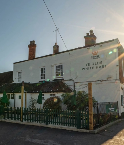 The exterior facade and beer garden seating area of The White Hart, with wooden picnic tables and shade umbrellas.