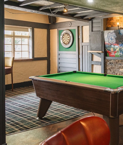 Interior seating area of a pub with a TV, a fireplace, a pool table and a dartboard.