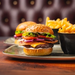 Two servings of plated burgers with fries in a small bowl on a table.