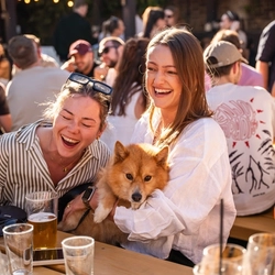 A close up image showing a group of people, one holding a dog sat at a table within the exterior beer garden seating area enjoying drinks at The Wandle.