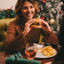An image of a group of friends sat at a table enjoying festive main dishes and various drinks within the interior restaurant seating area at a Proper Local venue.