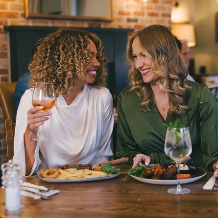 Two women seated at a wooden table, enjoying a meal and drinks.