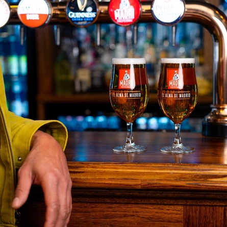 Two pints of Madri on a bar next to a man's arm.