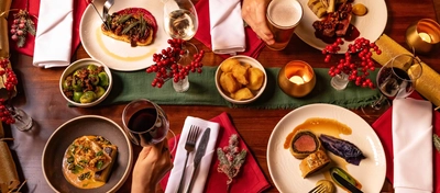 A close up overhead lifestyle image showing 4 people sat at a table enjoying drinks and festive mains and side dishes at The White Horses.