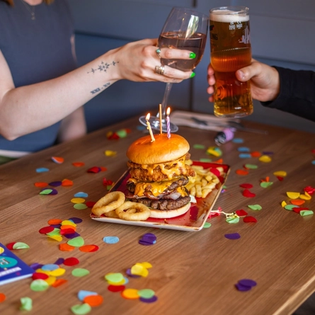 A Product lifestyle image of people enjoying a burger and drinks at an indoor seating area.