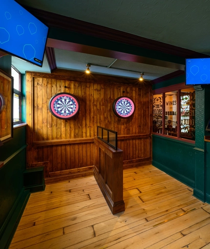 The interior games area at The Globe in Marylebone; with two interactive dartboards on a wood panelled wall.