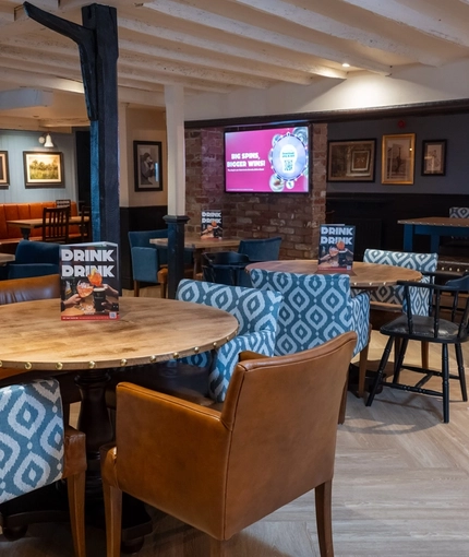 The interior restaurant seating area at The Vine Inn in Ower, with upholstered chairs, wooden beams, and a TV on the wall.