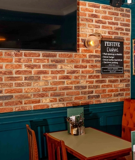 An interior restaurant seating area of the Lucas Arms in London, with upholstered booth seating and a TV on the wall.