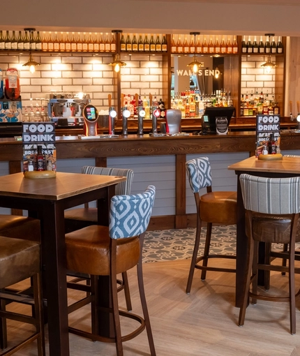 The bar and interior restaurant seating area at The Wall's End, with upholstered bar stool seating, and patterned tile flooring in front of the bar.