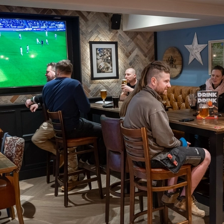 Guests sitting in the restaurant area inside the Cuckoo Oak, with drinks on the tables in front of them, some of them watching football on the TV.