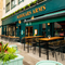 The exterior facade, signage, and seating area at the Scholars Arms in Southampton; with large green awnings hanging above the windows, and wooden planter boxes filled with plants.