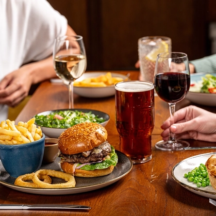 A hand holding a glass of wine on a table with two plates of food in front of it.