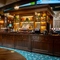 The wood panelled bar inside the Old School House in Aberdeen, with TVs on the wall above it, and bottles of alcoholic spirits on illuminated shelves behind the counter.