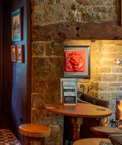 An interior restaurant seating area at The Red Lion; with wooden beams on the ceiling, stone walls, and a fireplace.