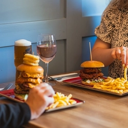 A group of people sat at an indoor table, enjoying a burger and drinks.