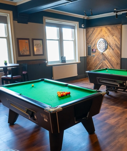The interior games area at The Victoria in Lytham St Annes, with two pool tables, a TV on the wall, and a dartboard in the corner.