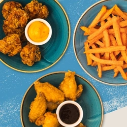 A group of dishes including chicken wings and fries served to advertise sport snacks on offer at Flaming Grill venues on a textured blue background.