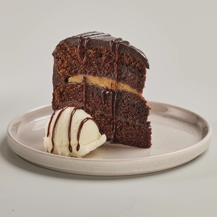 A slice of Chocolate Fudge Cake drizzled with sauce and served on a plate with a scoop of ice cream.