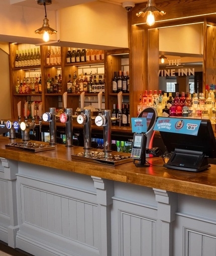 A close up view of the bar at The Vine Inn in Ower, with bottles of wine and alcoholic spirits on wooden shelves behind the counter.
